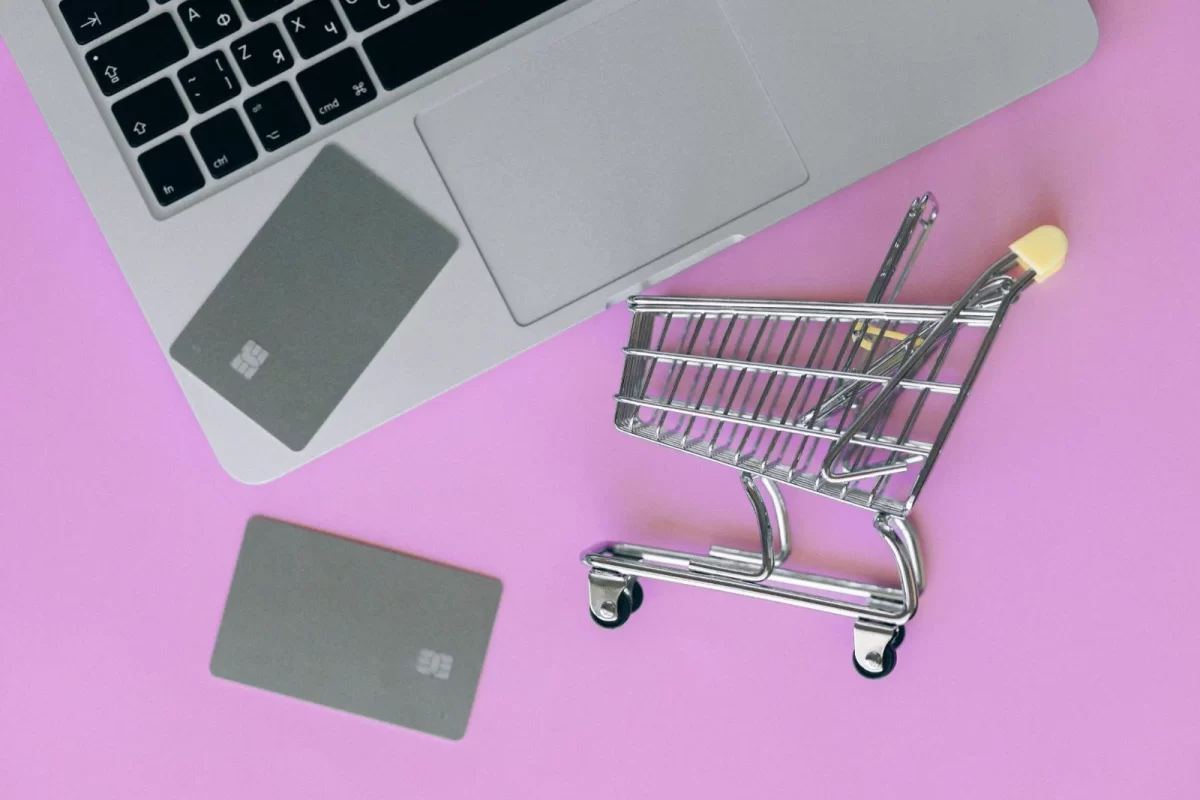 Mini shopping cart and bank cards beside a laptop