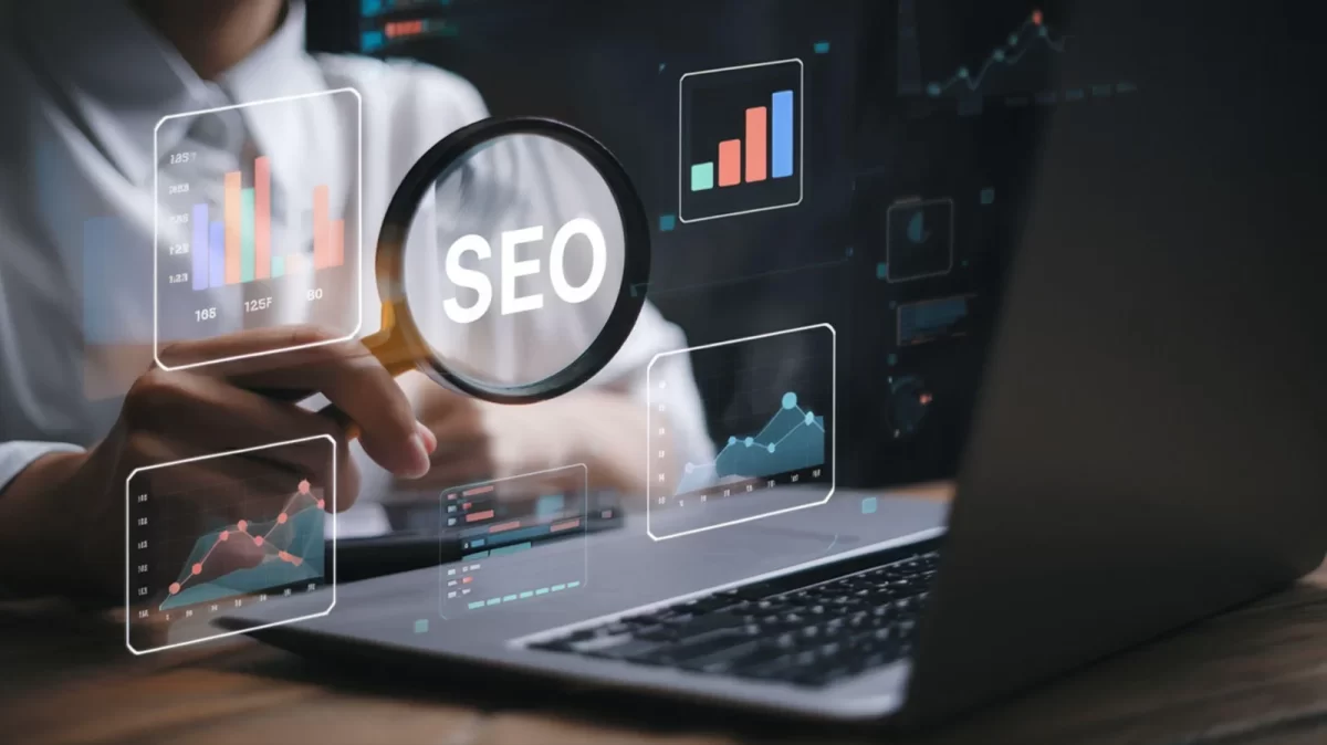 Person using a laptop with an SEO magnifying glass and analytics charts overlay