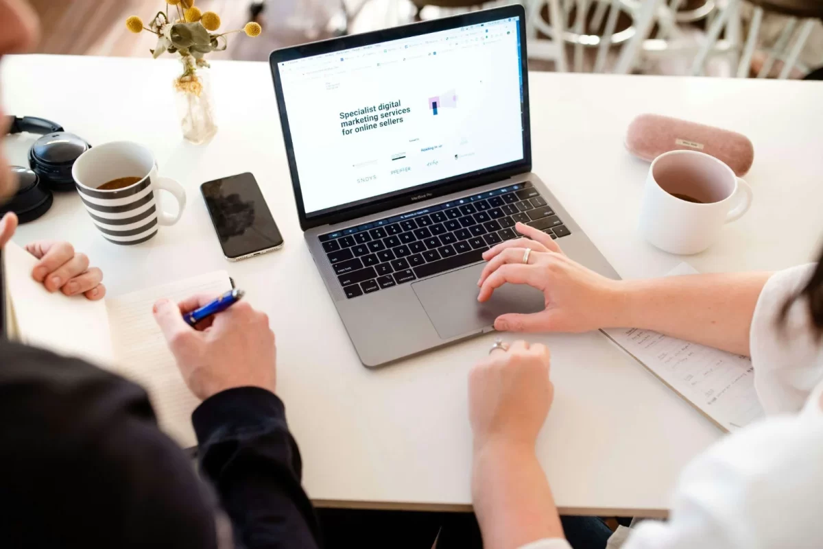 Two people working at a desk with a laptop showing a website